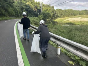 川沿いの道路でごみを拾いながら歩く社員たち